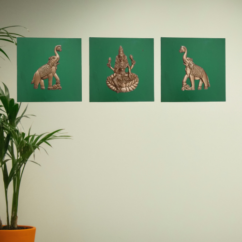 Three decorative wall hangings of elephants and a deity on green panels against a light green wall.